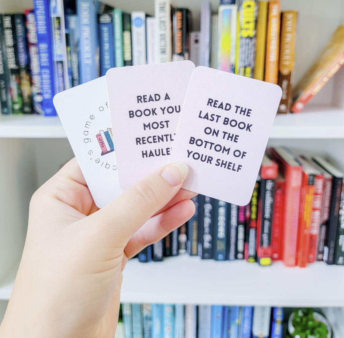 TBR game cards with book spines on the front and prompts such as "read a book you most recently hauled" and "read the last book on the bottom of your shelf."