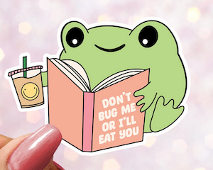 a sticker of an illustrated frog reading a book that says "don't bug me or I'll eat you"