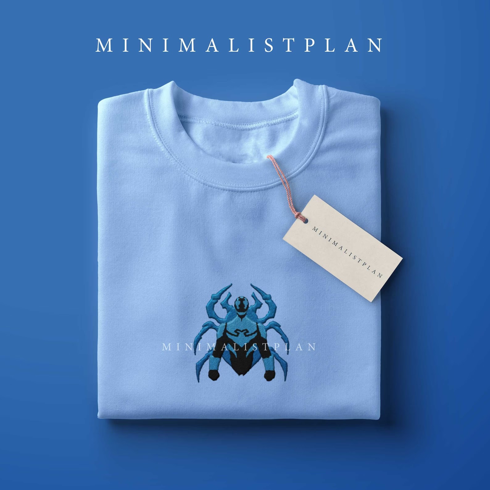 A folded, light blue sweatshirt with Jaime Reyes as the Blue Beetle embroidered into the front