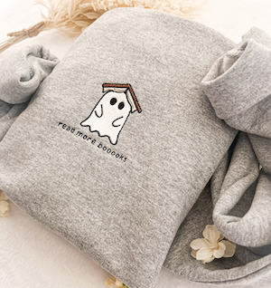 a grey sweatshirt with an embroidery of a ghost with a book on its head and text saying read more boooooks