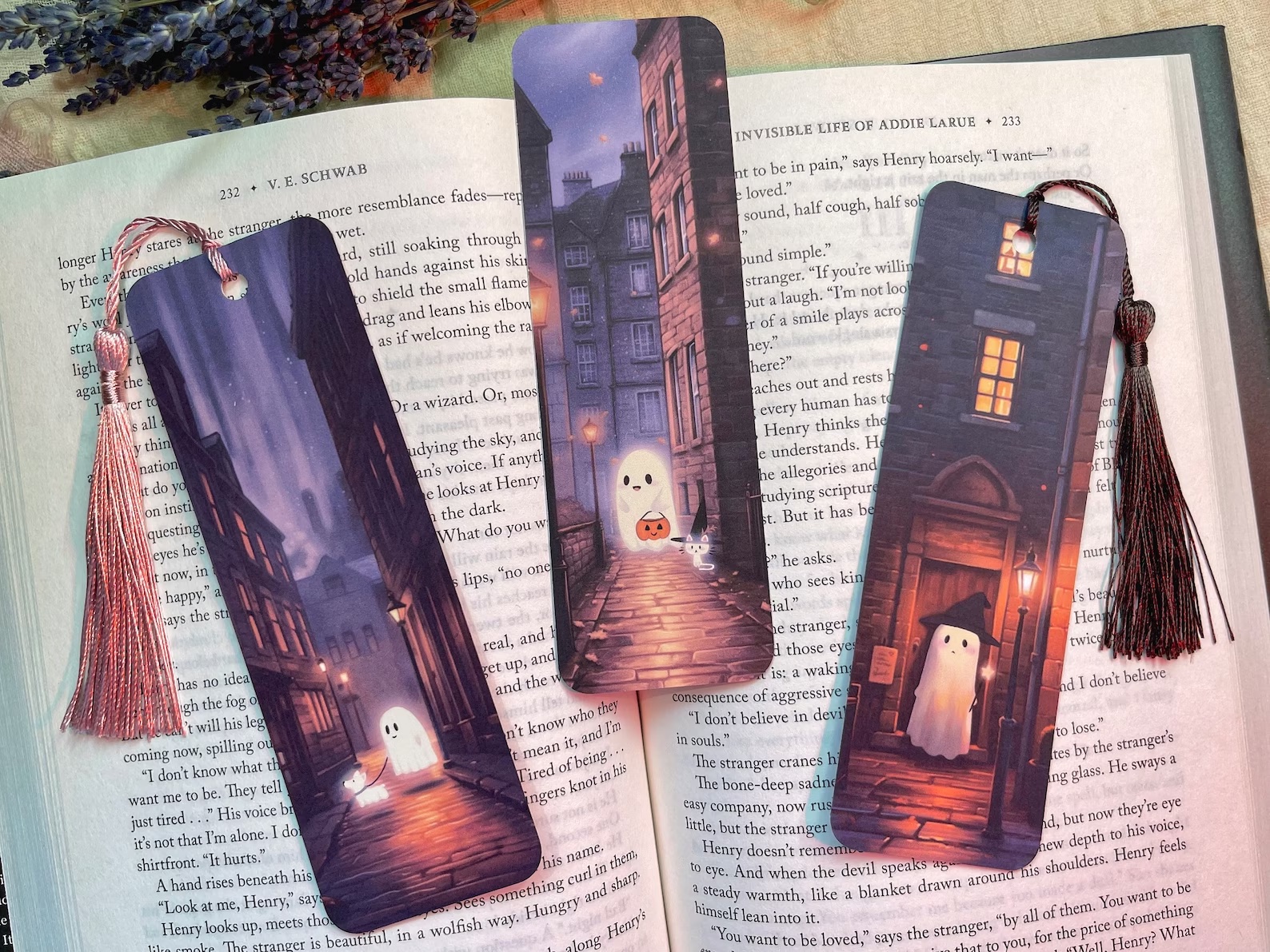 a photo of three bookmarks that each feature a ghost on a background of Edinburgh buildings. One ghost has a ghost cat. Another ghost has a ghost dog. The third ghost is wearing a hat and holding a wand.