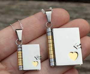 two sizes of a silver book charm with a cutout heart on the cover showing gold pages inside
