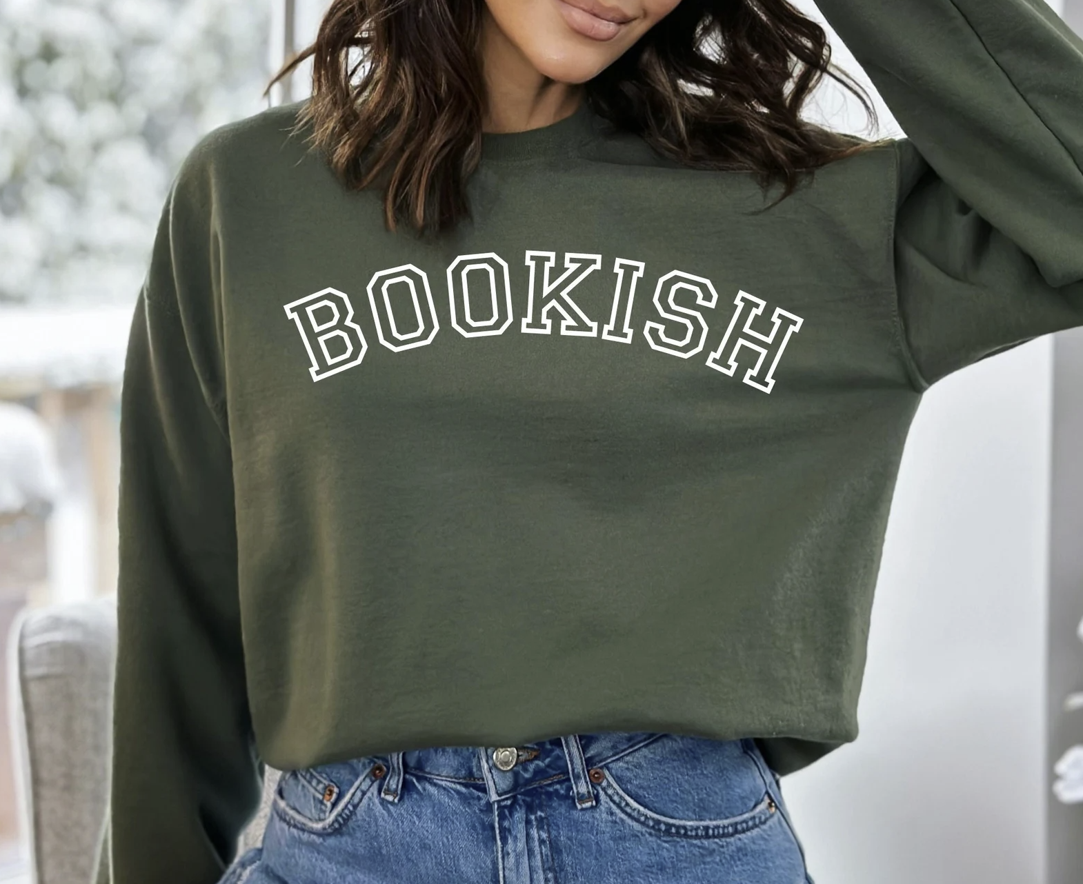 Woman wearing a forest green sweatshirt with white outlined text reading "Bookish" 