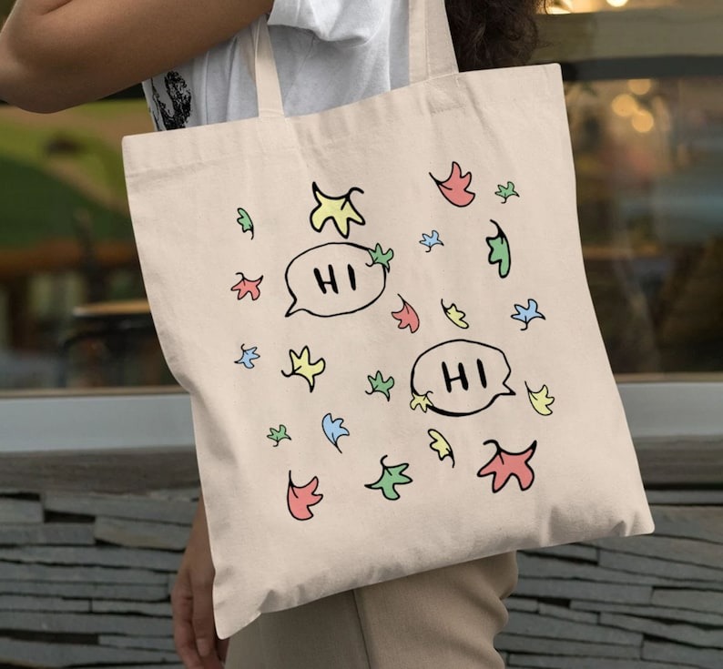 a photo of a Heartstopper totebag with colorful leaf illustrations and speech bubbles saying "hi" and "hi"