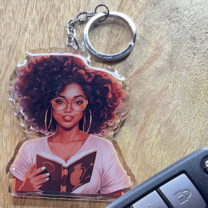 a keychain of an illustration of a young Black woman in glasses holding a book