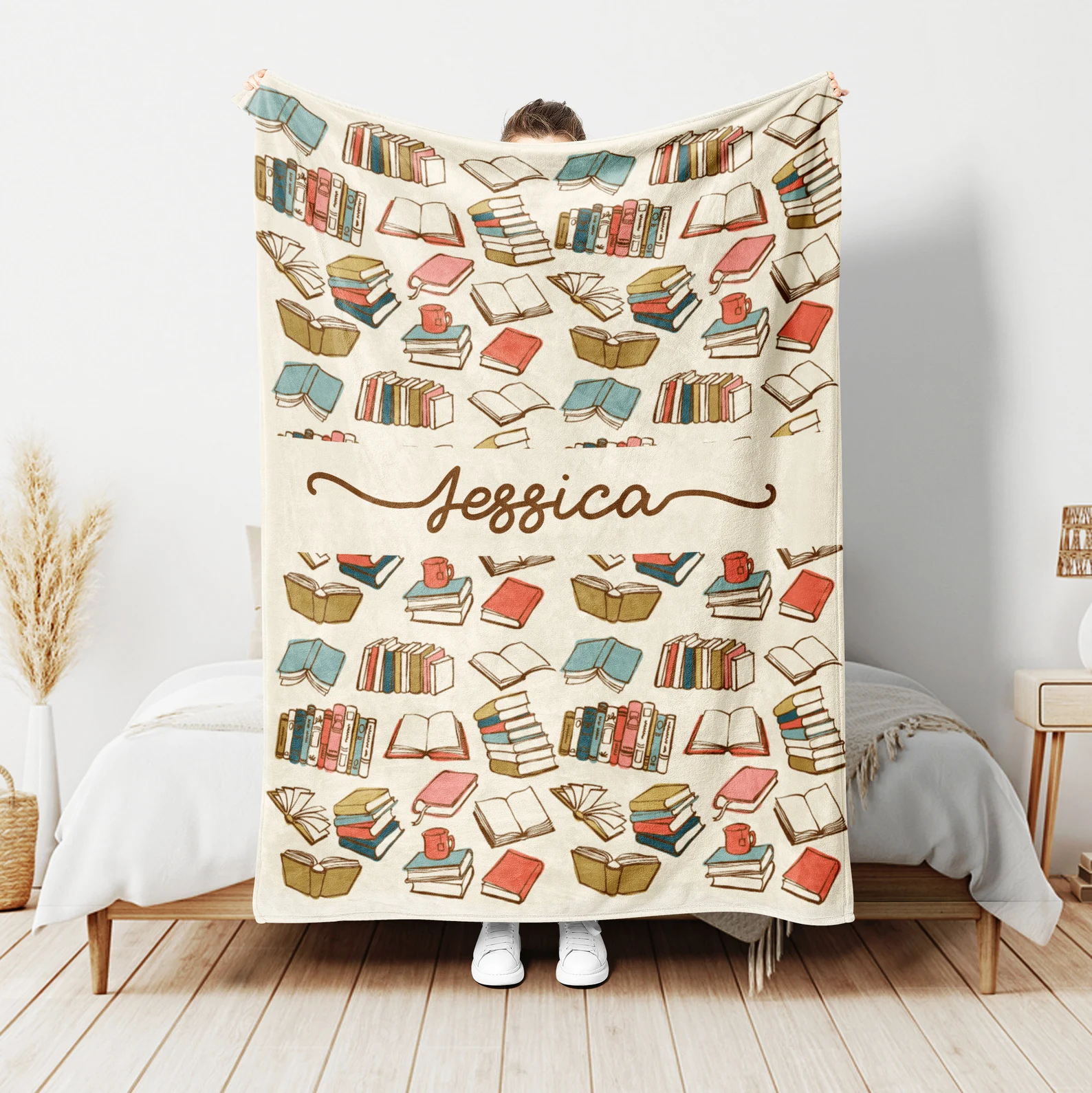 a photo of someone holding up a blanket featuring books designs and the name "Jessica"