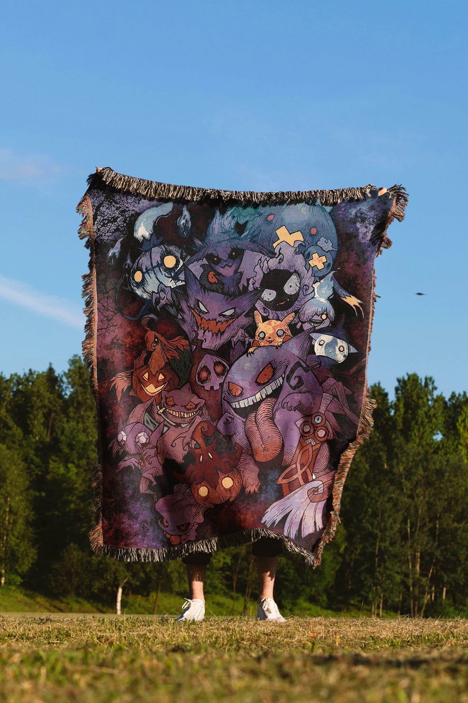 An unseen person holds up a large throw blanket featuring various ghost type Pokemon
