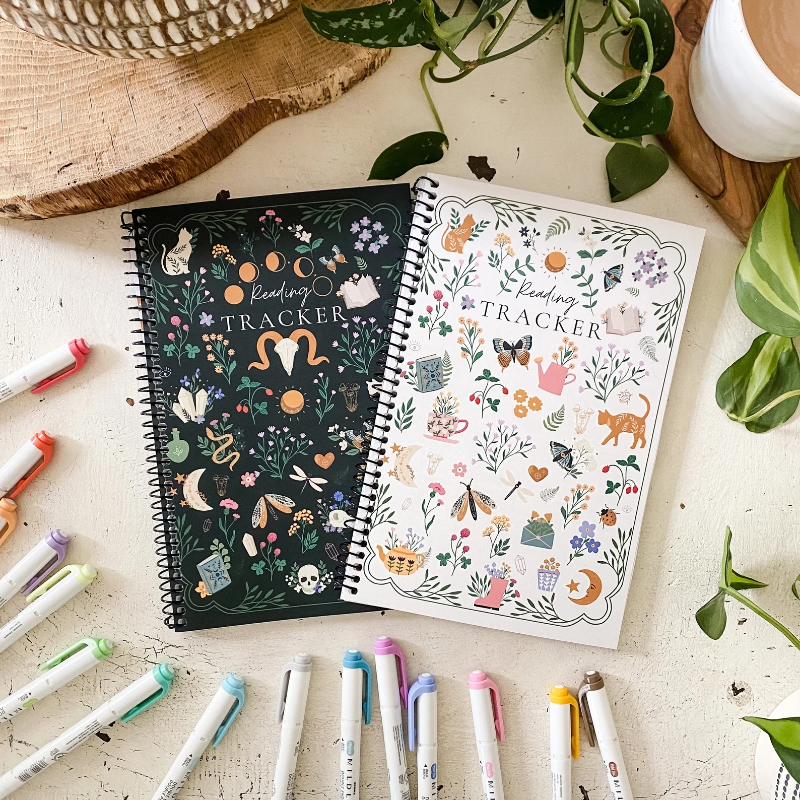 a photo of two spiral notebooks with the words Reading Tracker, one with a black background and one with a white background. They are both covered in little symbols that spark the imagination.