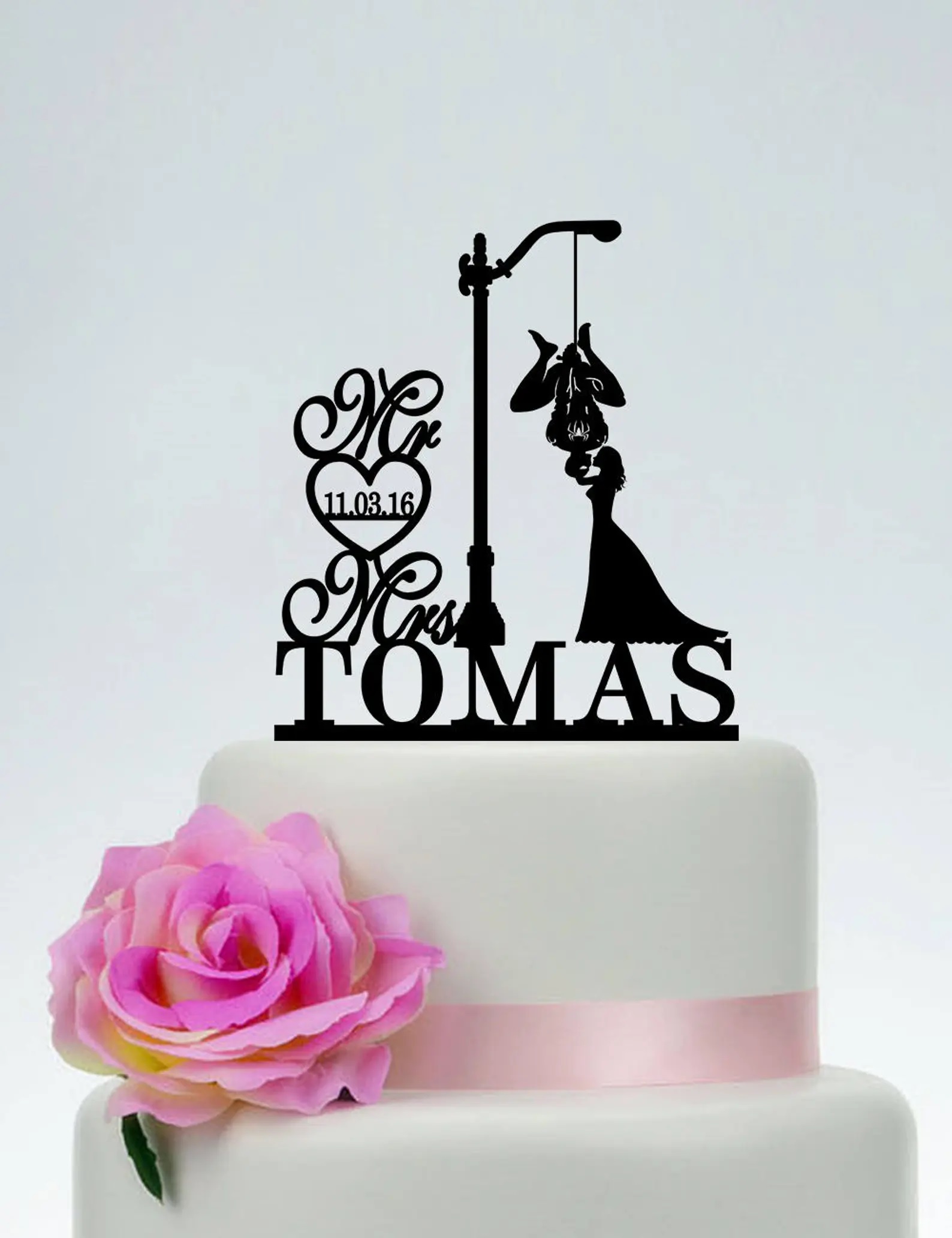 A silhouette cake topper featuring a woman in a long dress kissing Spider-Man, who is hanging upside down from a lamppost beside the couple's name and wedding date
