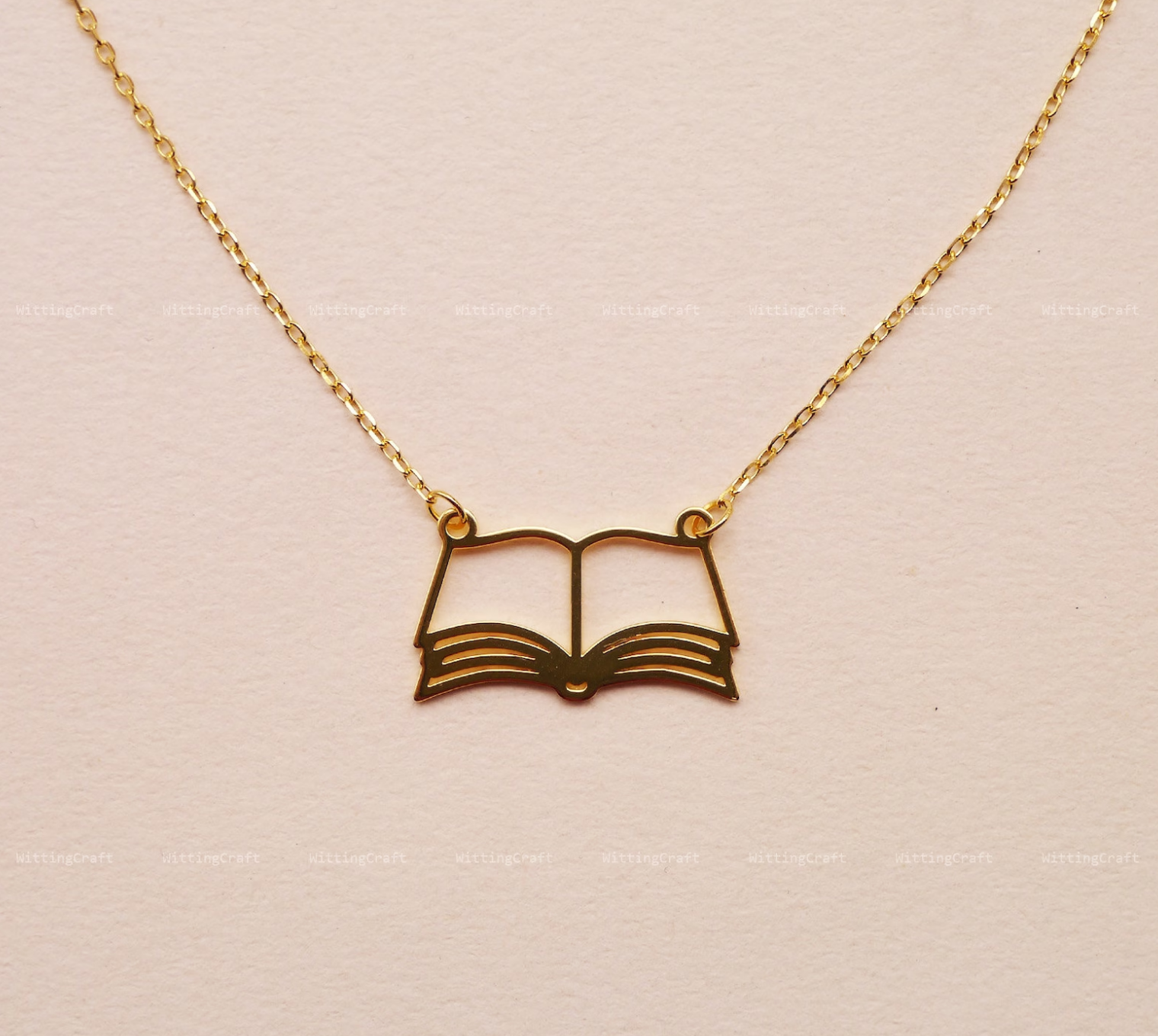 Gold book outline necklace featuring an open book with a gold chain connected to either side. 
