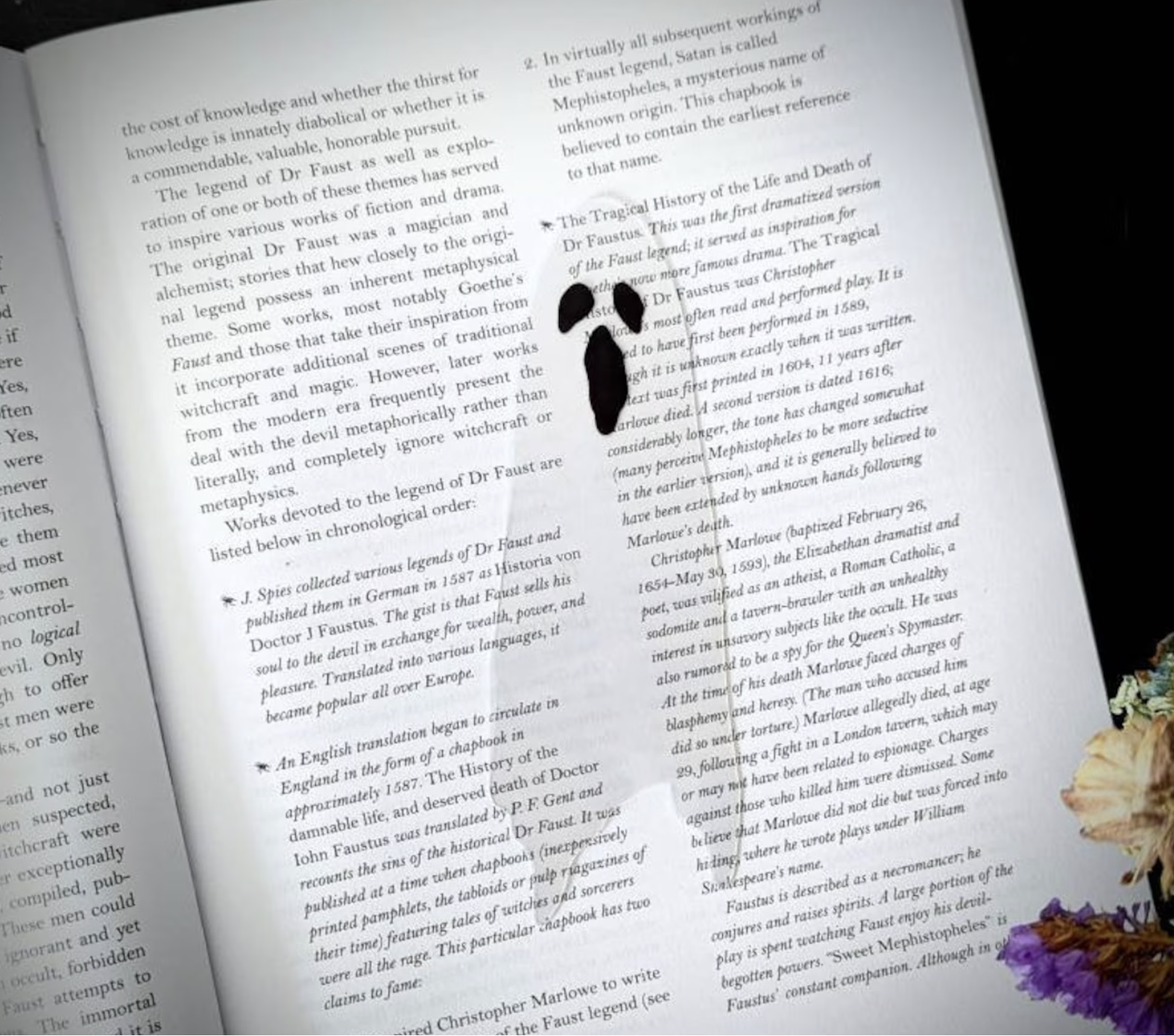 A see-through ghost bookmark with gaping black mouth and black eyes rests on a book. The text of the book can be seen through the ghost bookmark. 