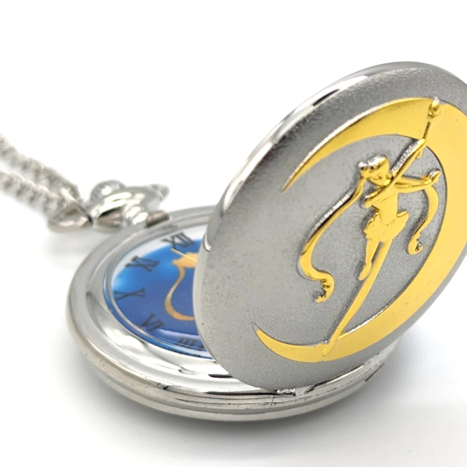 A silver pocket watch with a golden silhouette of Sailor Moon standing on a crescent moon on the outside. The watch face features the same pattern with the color blue in the background