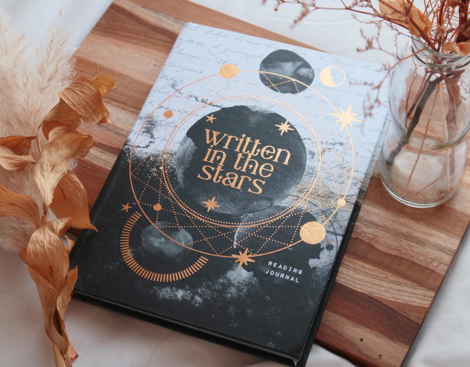 a photo of a reading journal sitting on a decorative cutting board. The cover is a blend of different color grays with metallic details embossed on the cover