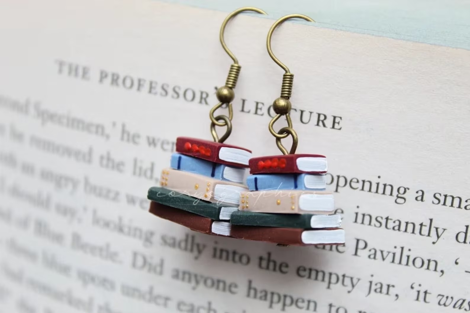 a photo of a pair of earrings. Each earring is a stack of books with spines in all different colors