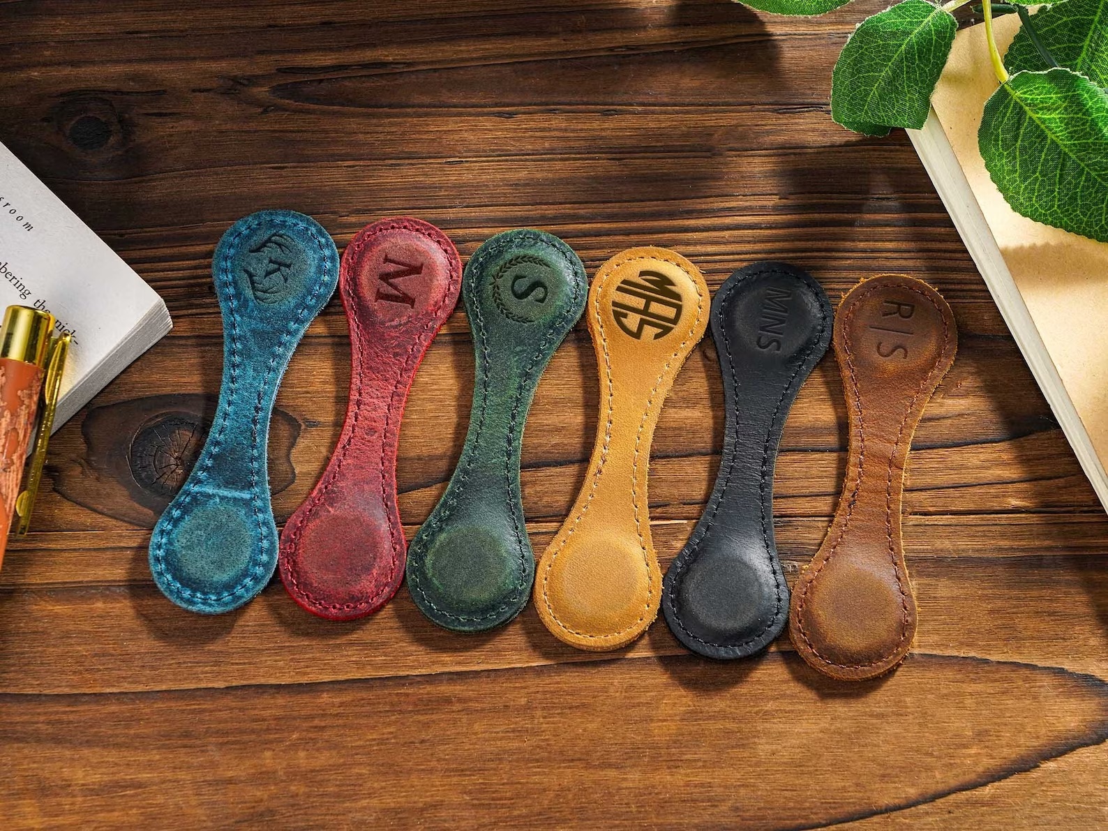 a photo of a row of colorful leather bookmarks that close over the top of the page with a magnet. Different initials are embossed on the leather of each bookmark.