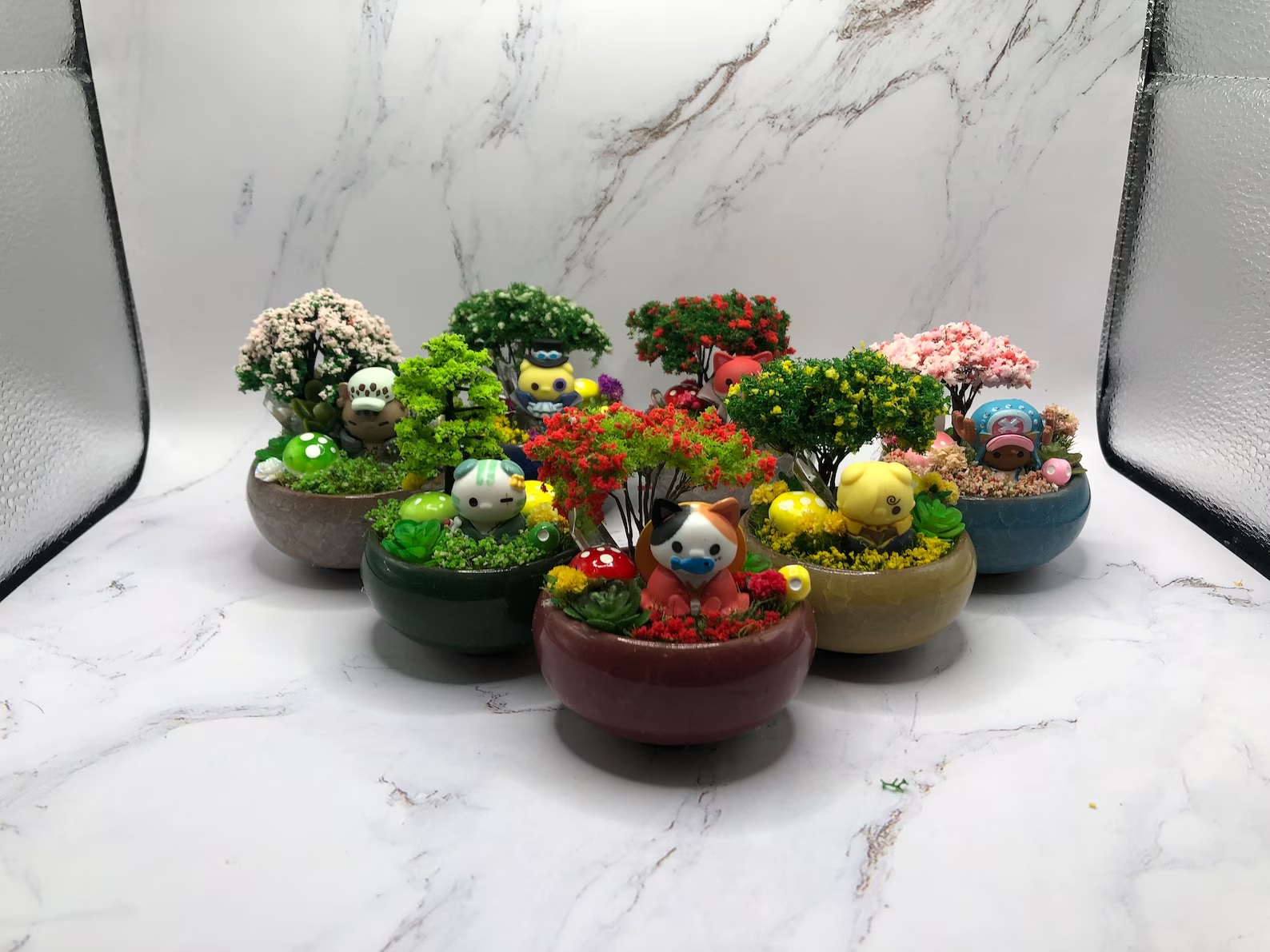 A grouping of small round pots, each a different color and containing different colored plants and kittens that reflect a different One Piece character