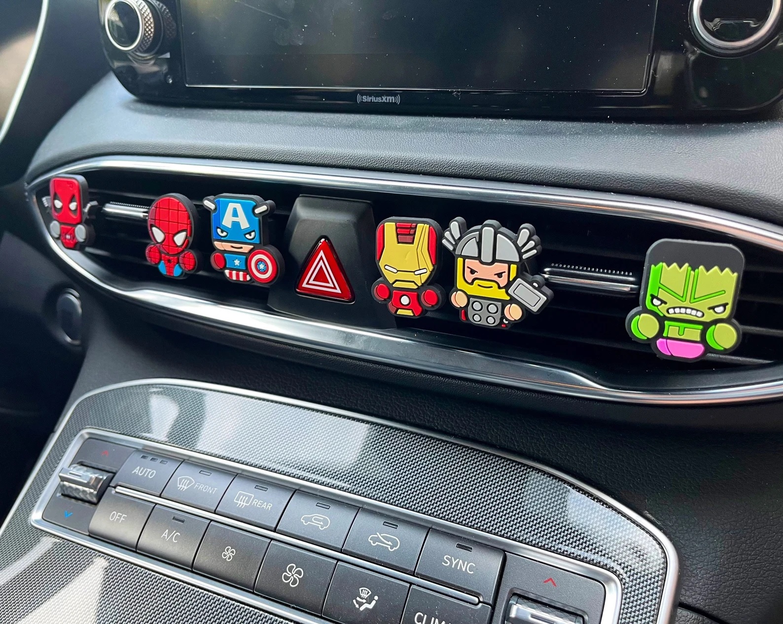 Small air fresheners, shaped like stylized images of popular Marvel heroes, clipped to a car's air conditioner