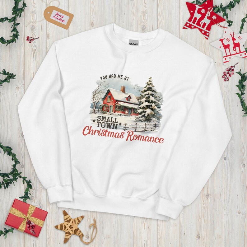a sweatshirt with a picture of a snowy cabin and the text "You had me at small town Christmas romance"