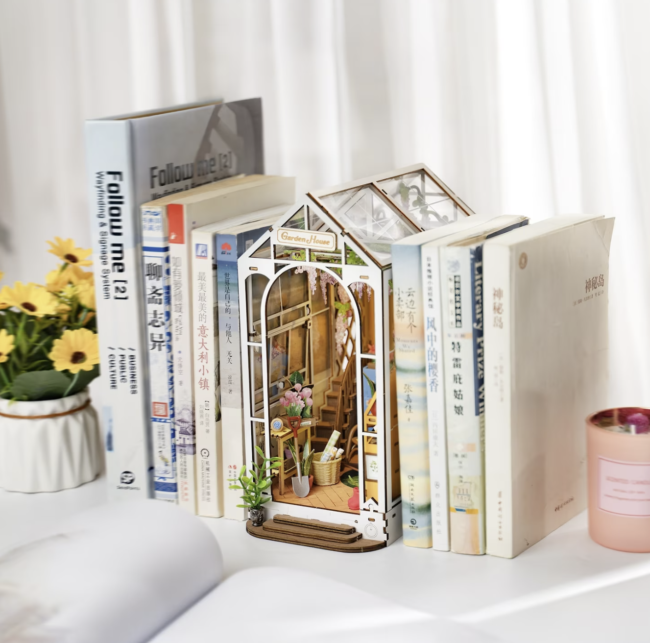 A series of white books lined up with a rectangular book nook in the shape of a greenhouse garden featuring lots of plants in between.