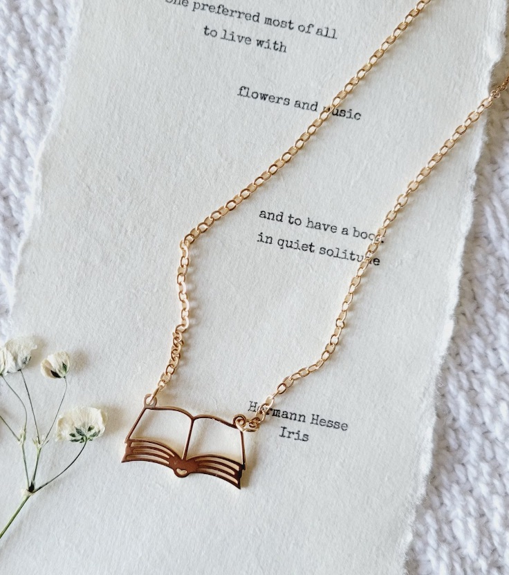 Image of a gold necklace with an open book pendant. 