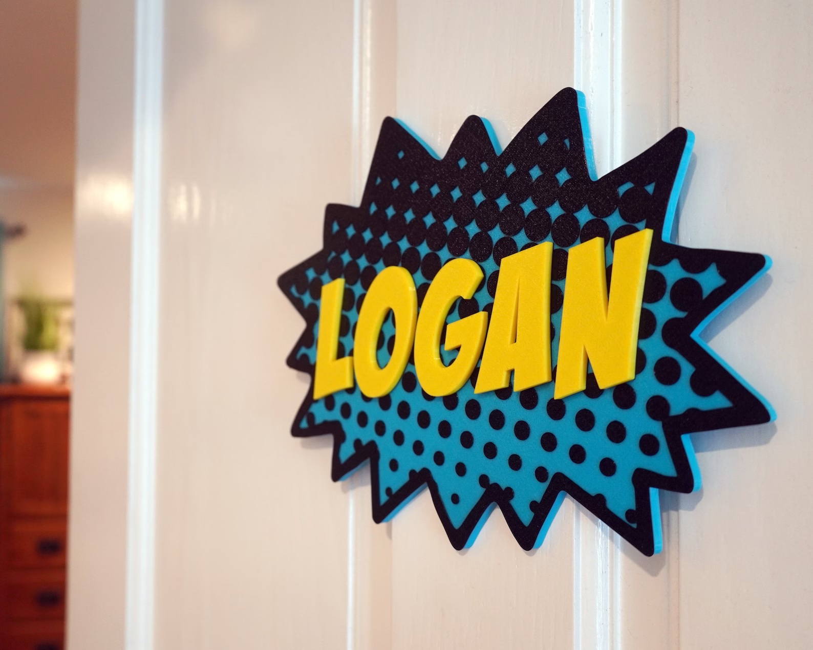 A blue sign shaped like the flash that accompanies a comic book-style onomatopoeia hangs from a wall. The name "Logan" is printed across it in bold yellow letters.