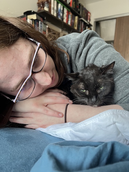 a woman with her arms wrapped around a black cat so that only the cat's head is sticking out