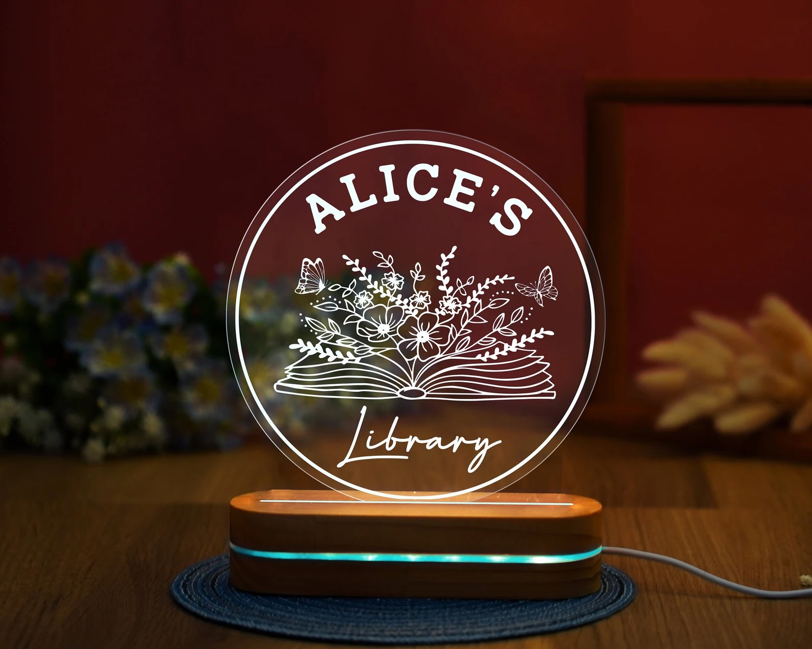 a photo of a night light that is made of of a plastic disk that says, Alice's Library. A wooden stand holds up the disk and issues the light.