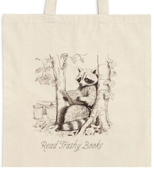 canvas tote bag with a screenprinted image of a raccoon reading a book that says "read trashy books"