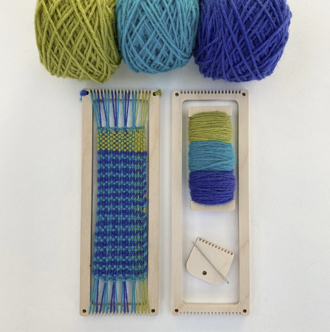 Miniature rectangular wooden loom for making fabric bookmarks, featuring green, teal, and blue yarn. 