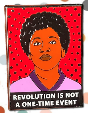 a rectangle enamel pin with a red background and illustrated image of Audre Lorde with the quote "revolution is not a one-time event"