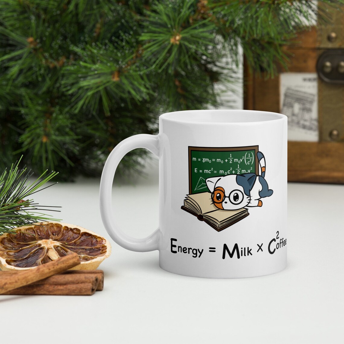 a photo of a coffee mug with an illustration of a cat wearing glasses and reading a book, with math equations behind them. The text reads: energy = milk x coffee 2