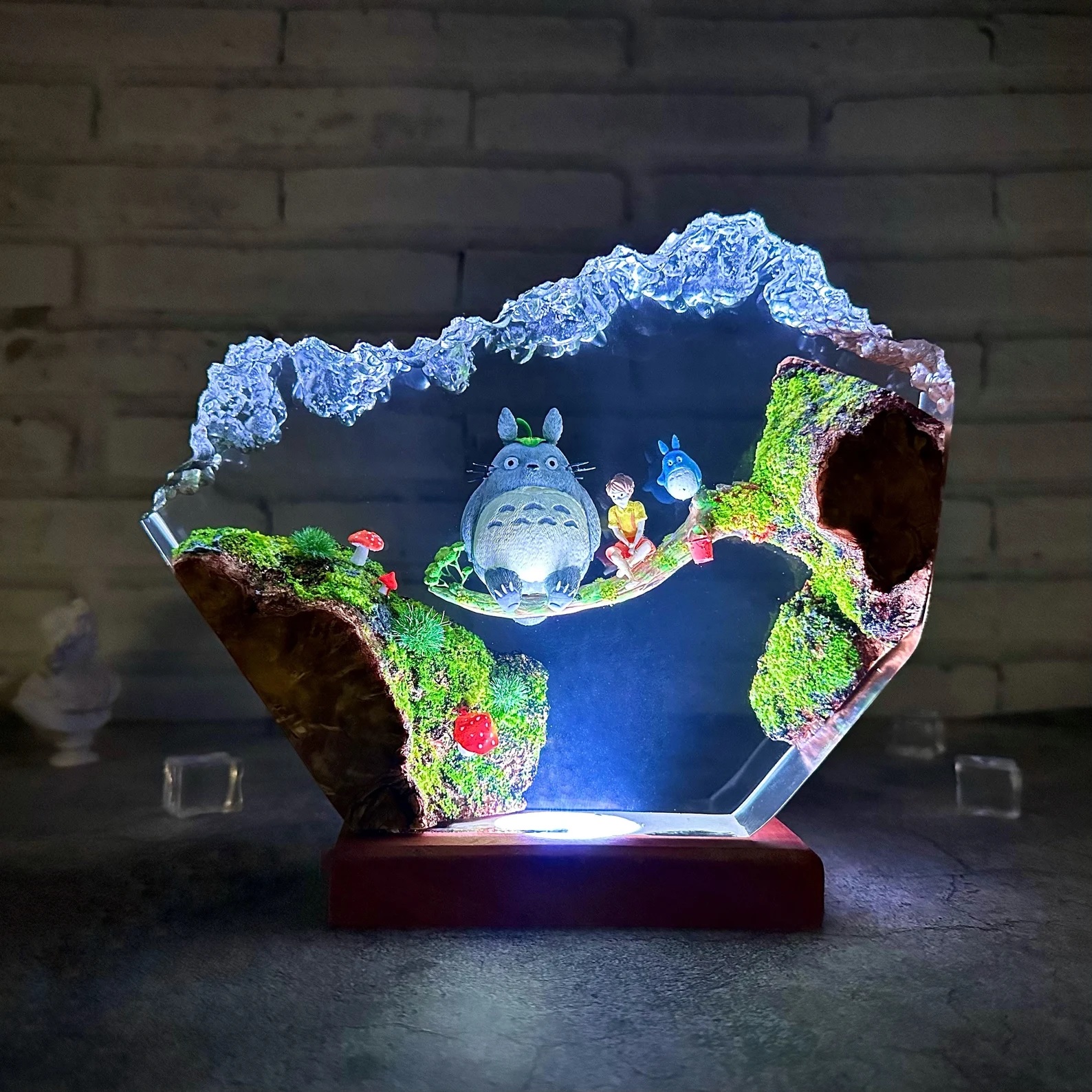 An irregularly shaped "rock" of epoxy resin, lit from the bottom, featuring characters from My Neighbor Totoro sitting on a branch inside of it