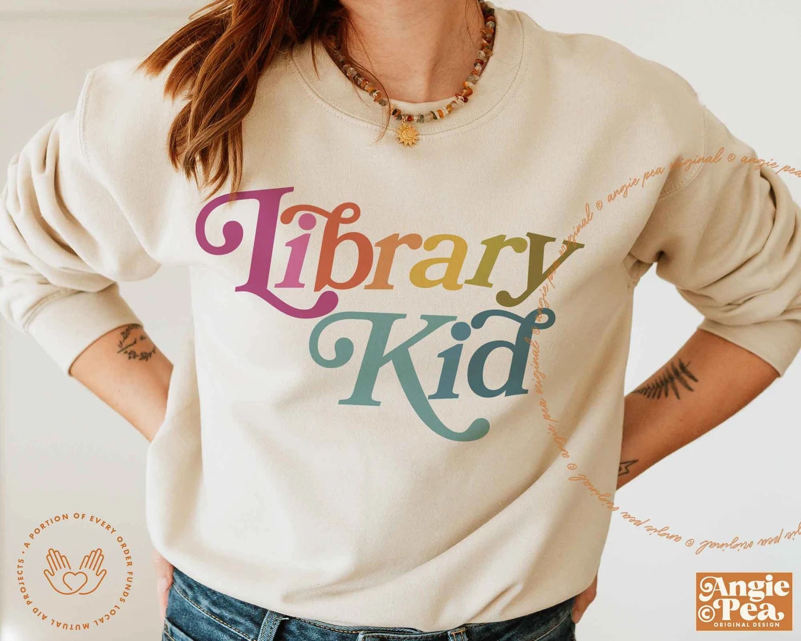 a photo of a white woman wearing a sand colored sweatshirt with the words "library kid" on it.