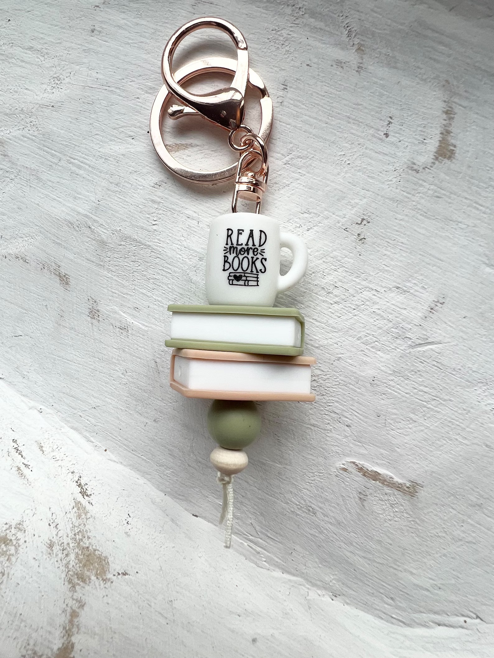 a photo of a little book bag keychain that features a stack of books with a little mug on it that says read more books