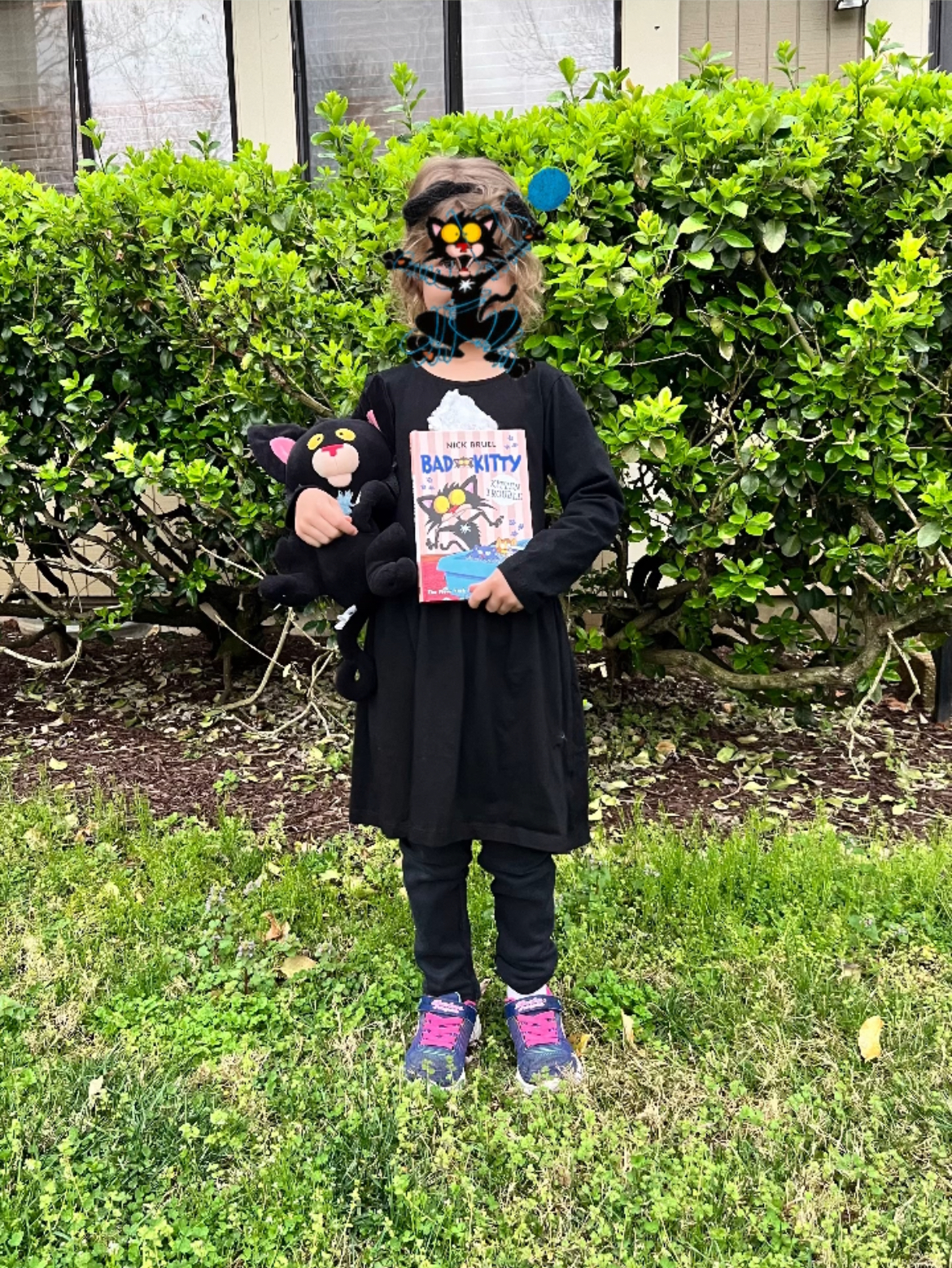  photo of a kid dressed up as Bad Kitty, holding a Bad Kitty book, with her face obscured with a Bad Kitty image