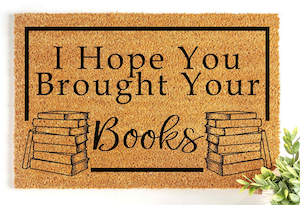 a doormat with an illustration of a book stack and text saying I hope you brought your books