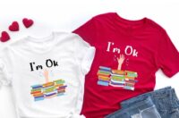 a shirt with a hand reaching up from being buried under stacks of books, accompanied by the text "I'm Ok"