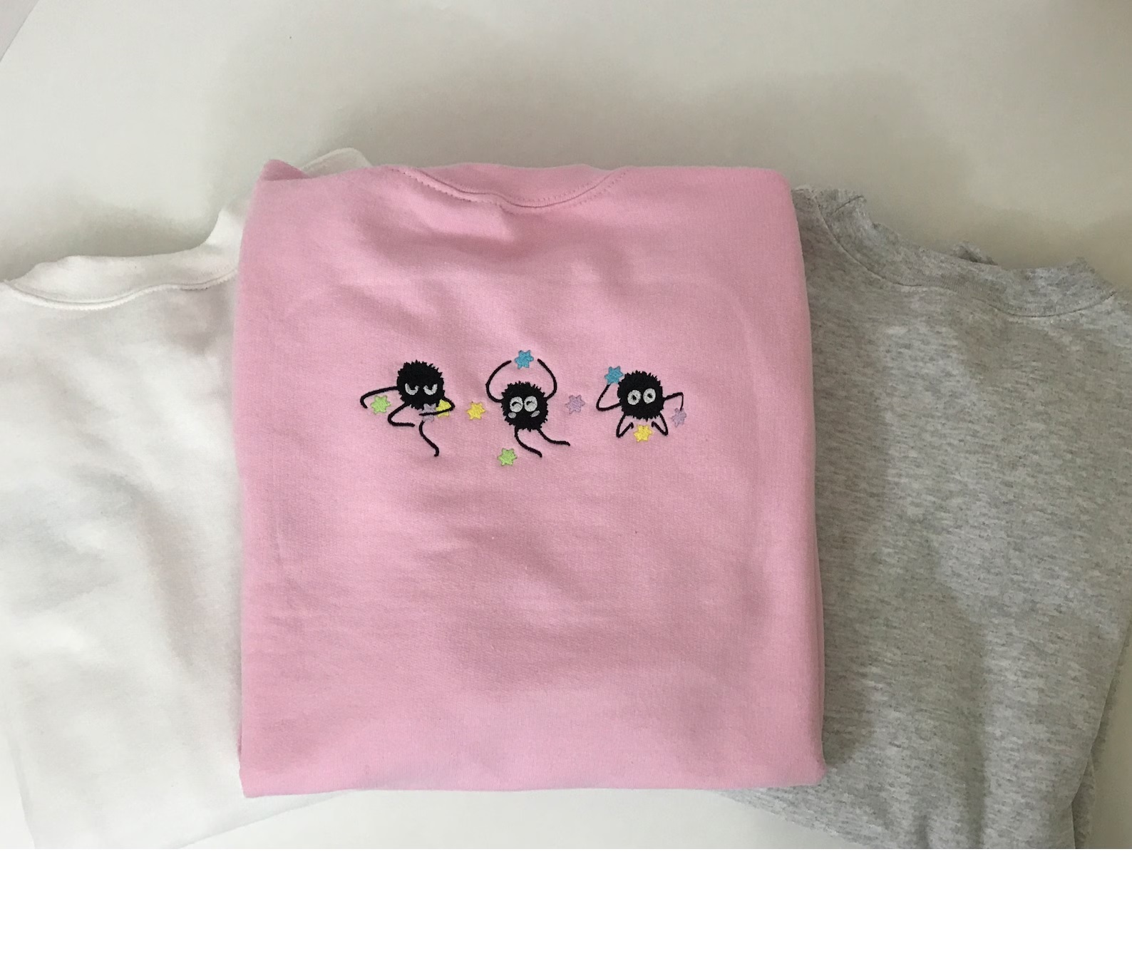 A folded pink sweatshirt featuring three soot sprites from Spirited Away