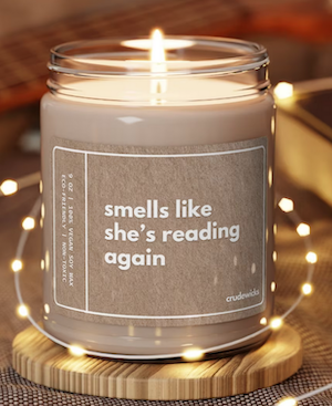 candle in a glass jar with white font that says "smells like she's reading again"