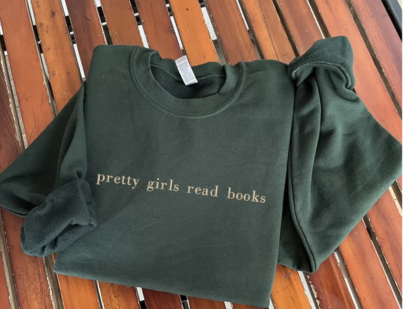 a photo of a dark green sweatshirt with the words "pretty girls read books" embroidried on the front