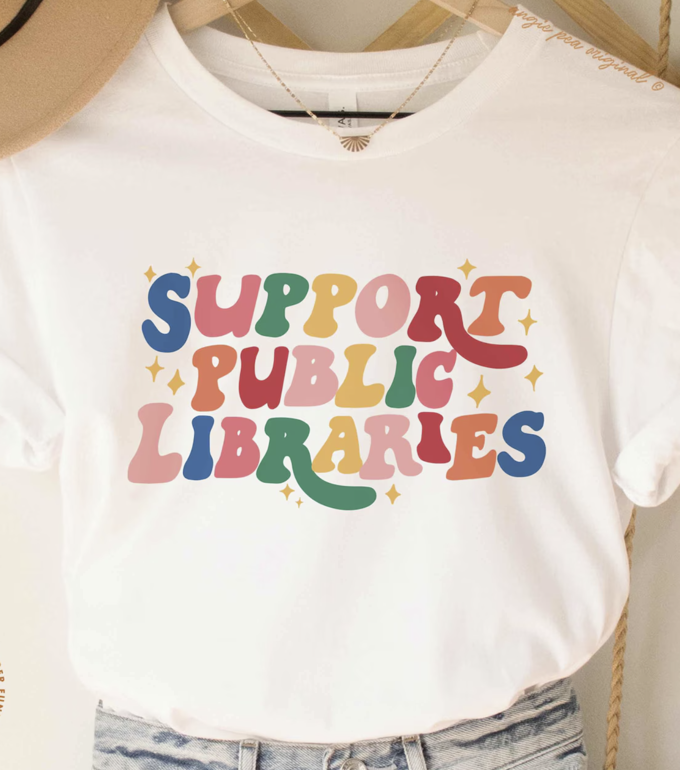 White shirt with rainbow bubble letters across the chest spelling out "Support Public Libraries"