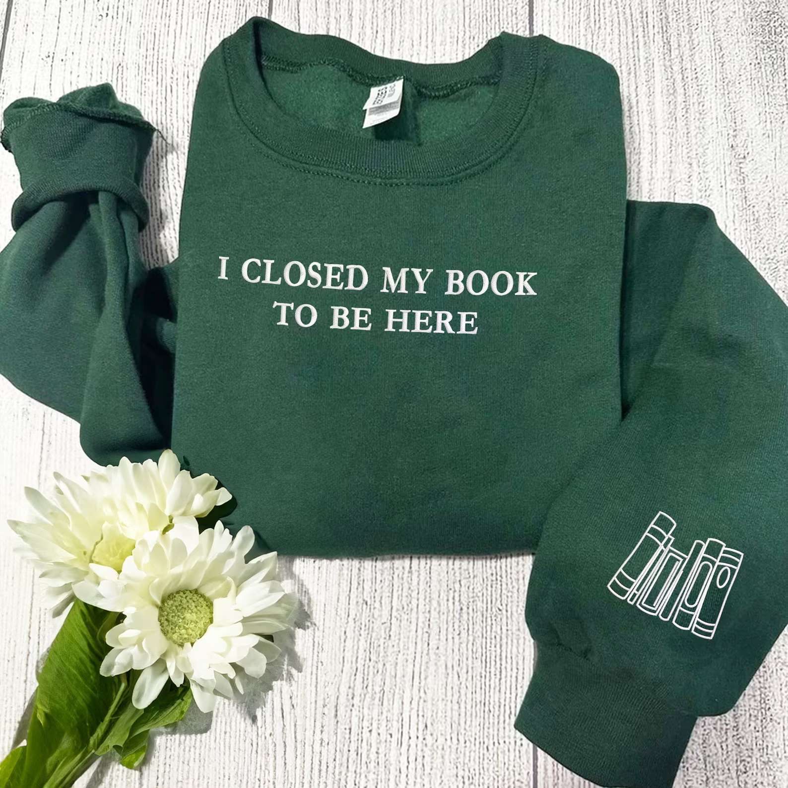 a photo of a dark green sweatshirt with white embroidery that says "I closed my book to be here."