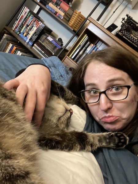 a brown tabby cat showing its tummy to a woman, who looks scared to pet the tummy