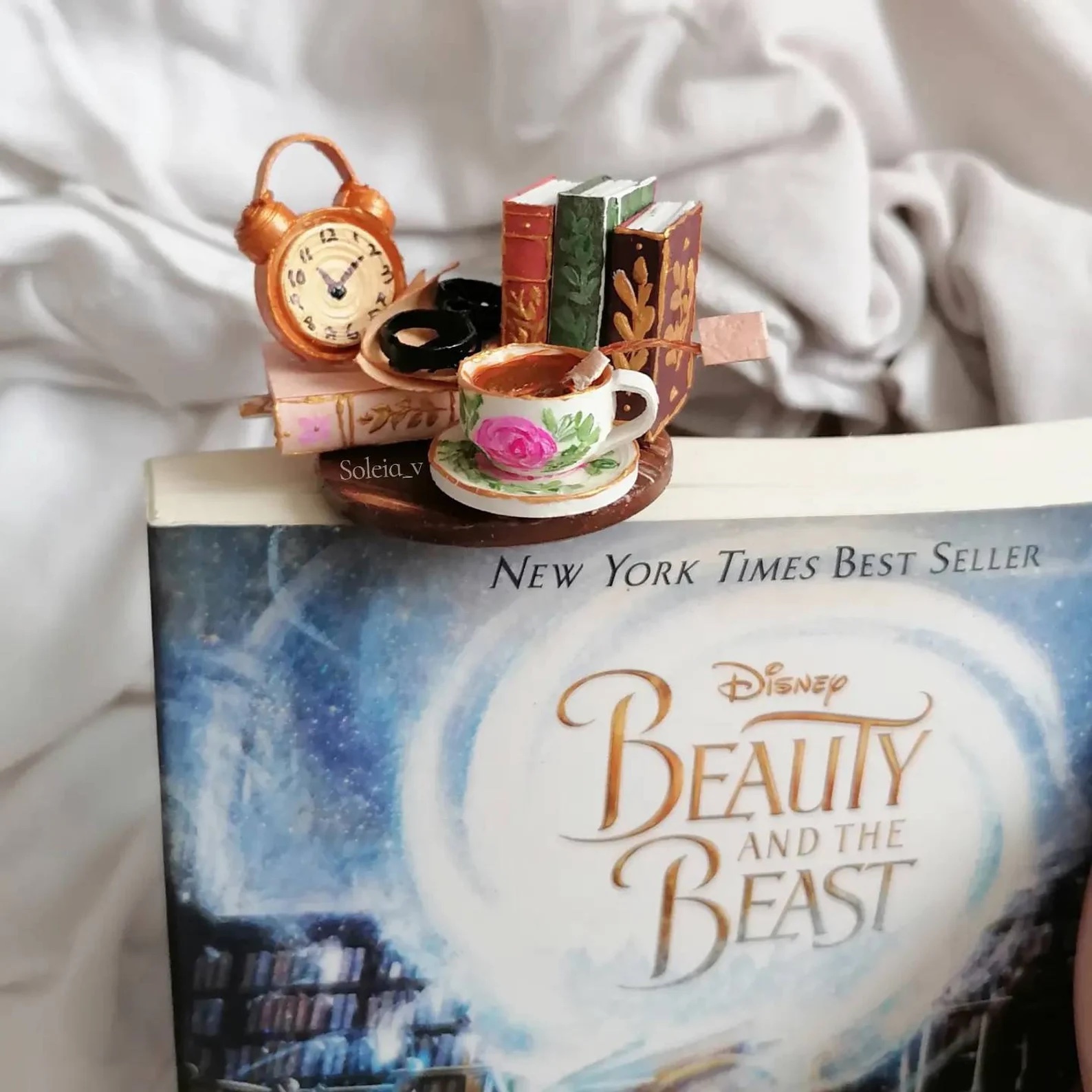 a photo of a bookmark with a clay model of tea cup, books, and a clock.