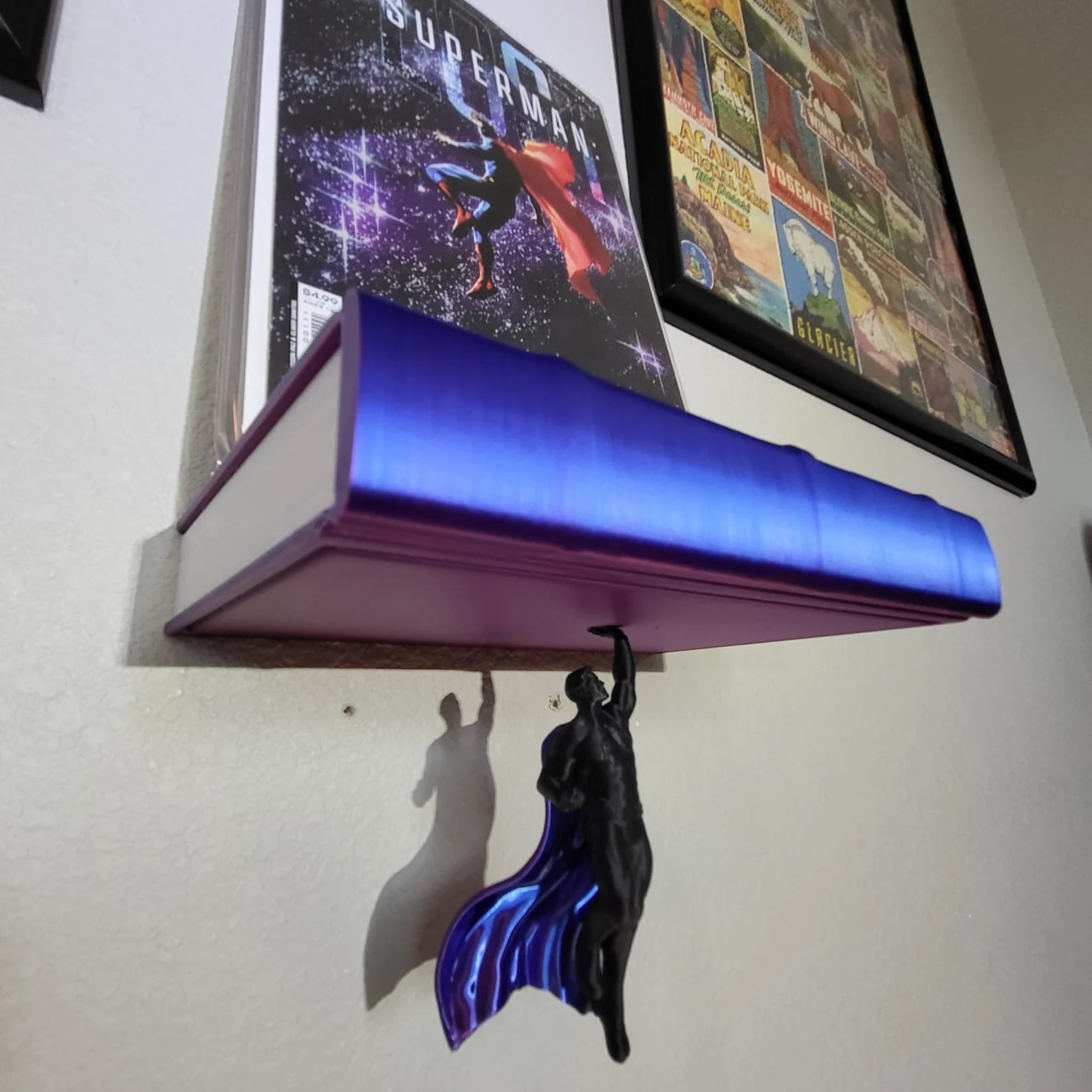 A blue, book-shaped shelf with a Superman comic on it. Below the shelf, a superhero figurine seems to float in midair, holding up the shelf.