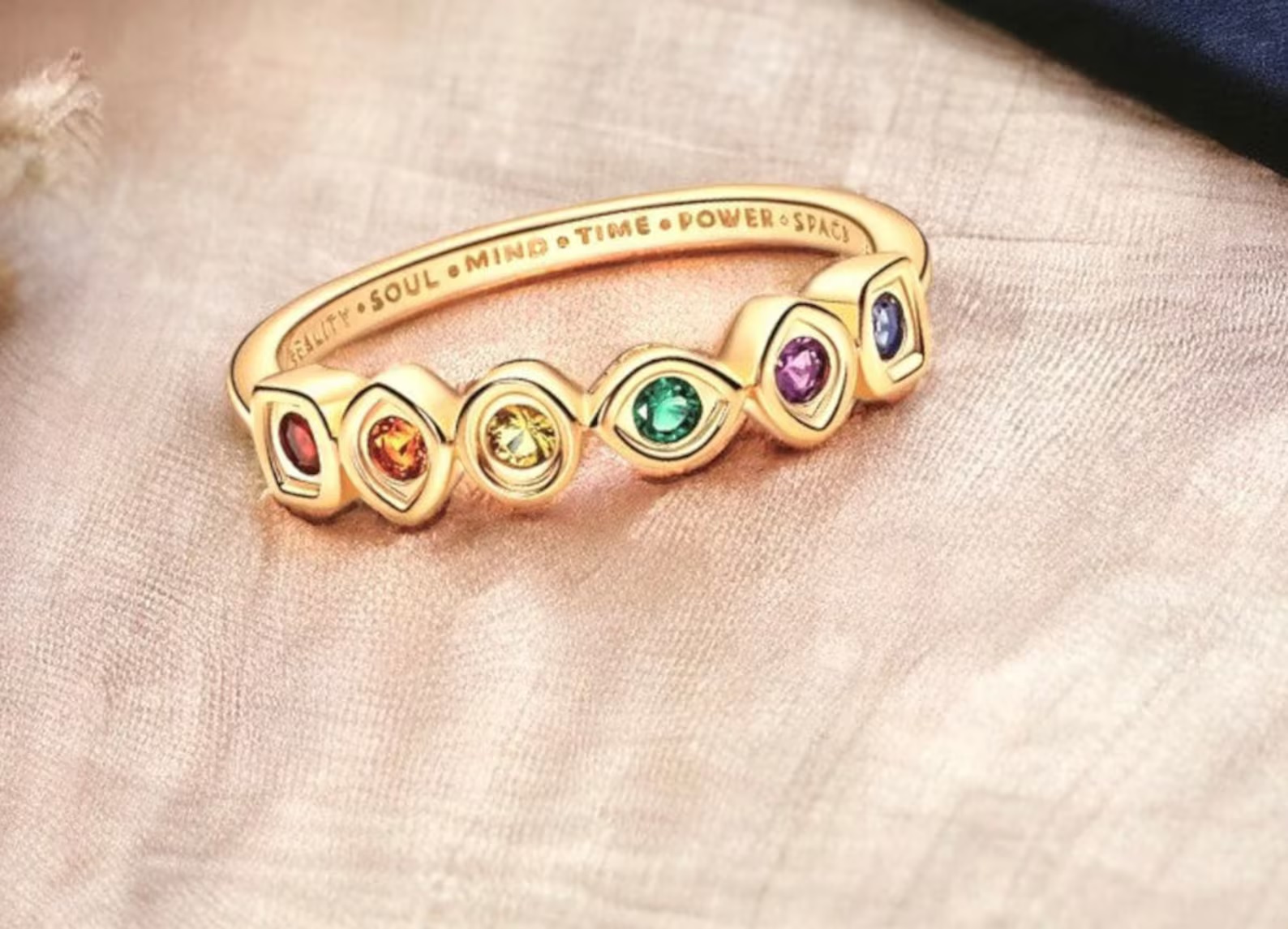 A gold ring with four gemstones that match the shape and color of the Infinity Stones. On the inside is inscribed the names of the stones.