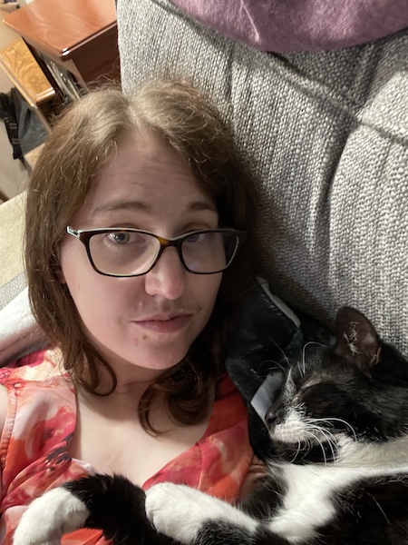 a black and white cat sleeping on Katie's chest, keeping her pinned to the couch