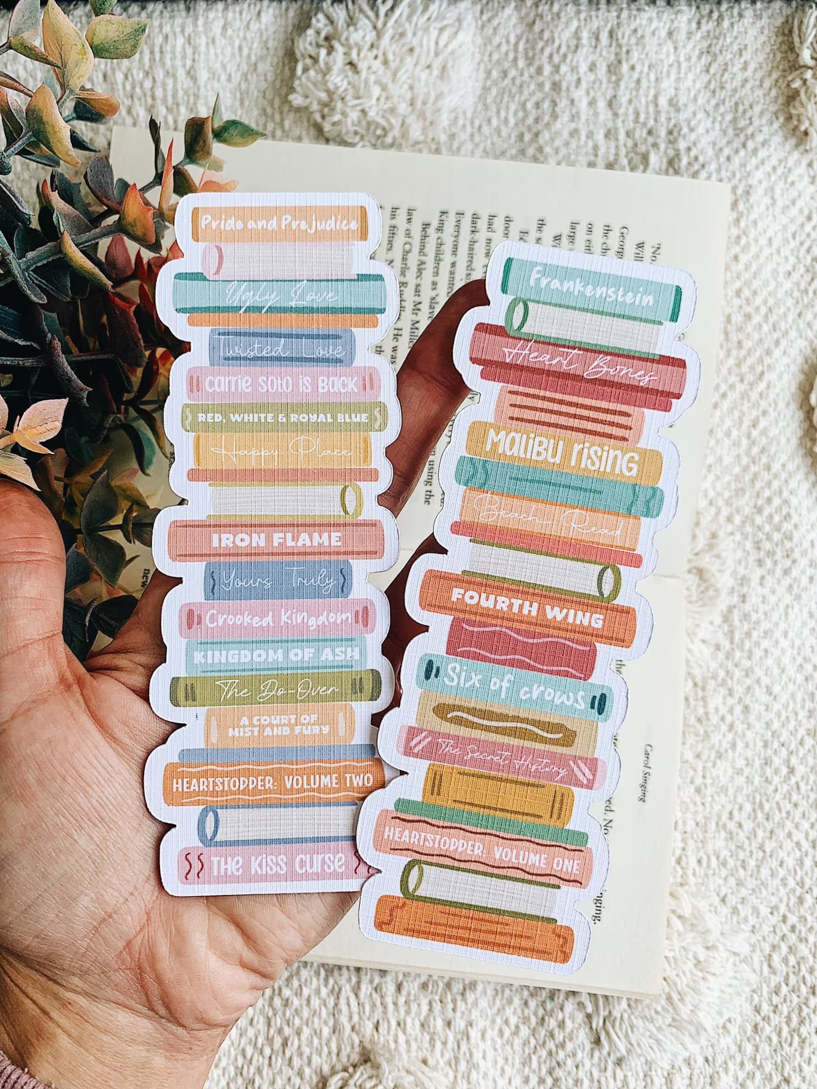 a photo of a linen bookmark featuring an illustration of a stack of books. you can customize the spines to say the titles of your favorite books