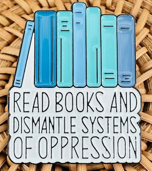 enamel pin of blue illustrated book spines with text saying "read books and dismantle systems of oppression"