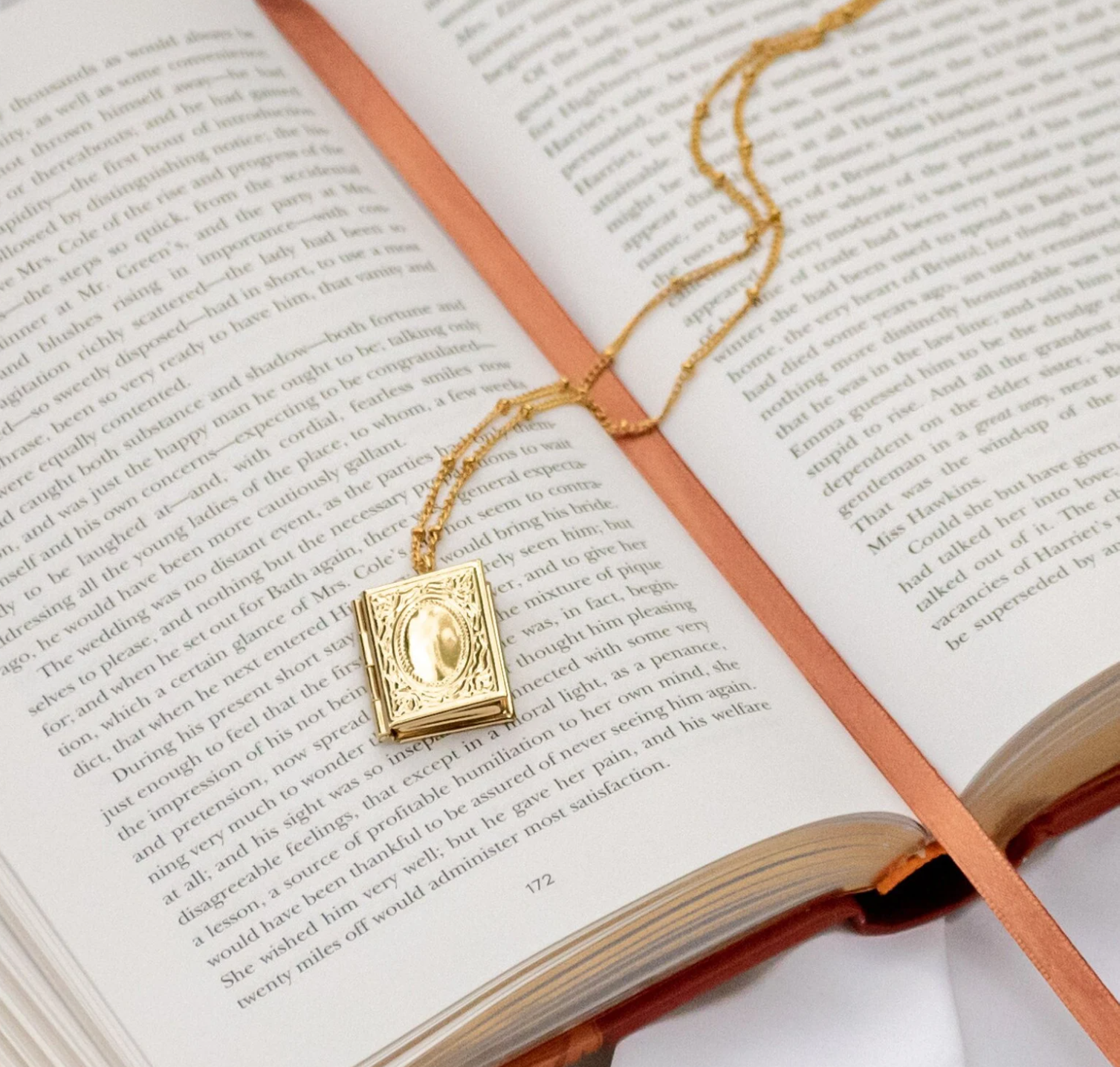 Image of a gold book shaped locked on a delicate gold chain draped against an open book.